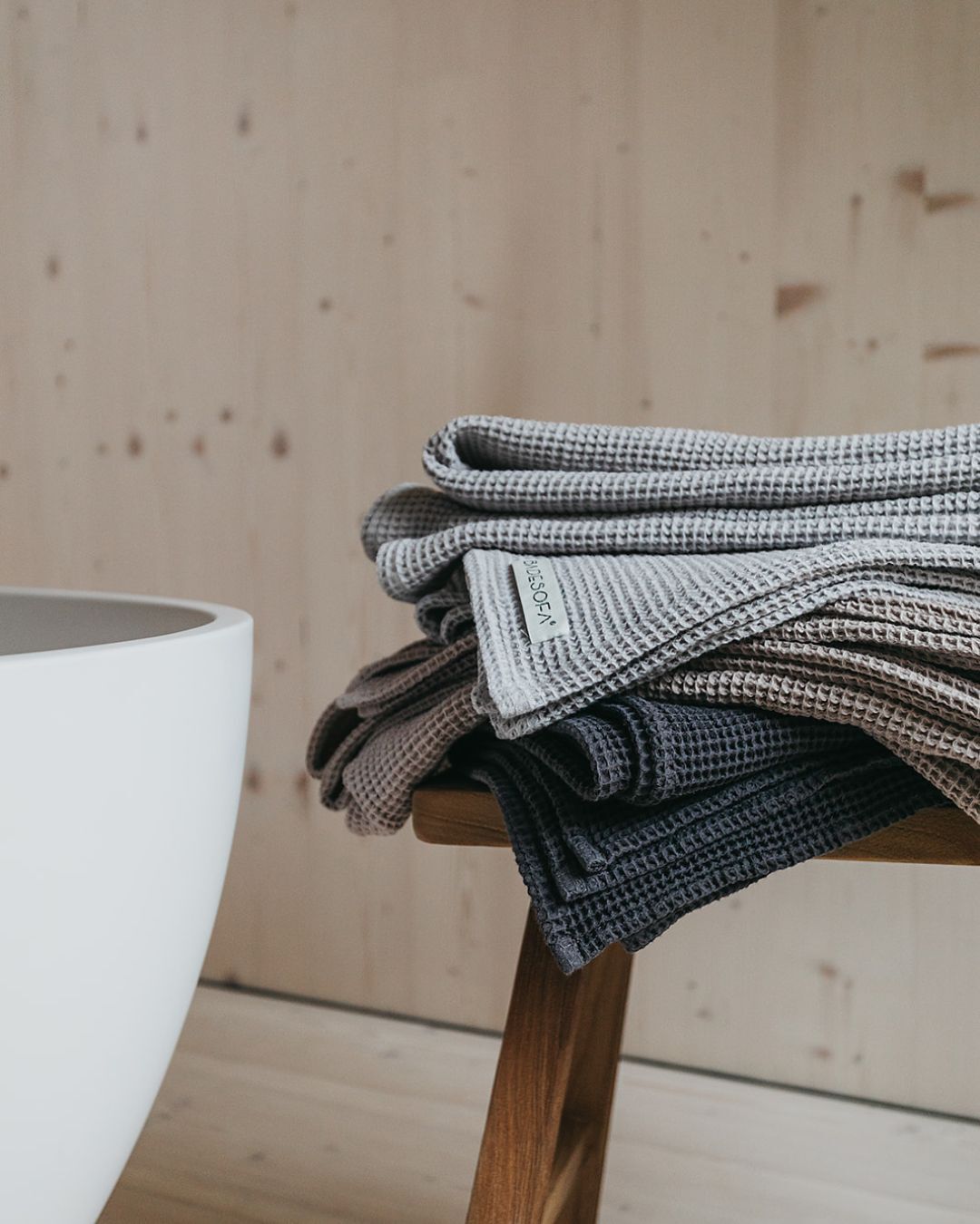Ein Stapel Saunatücher in unterschiedlichen Farben liegt auf einem Holzhocker.