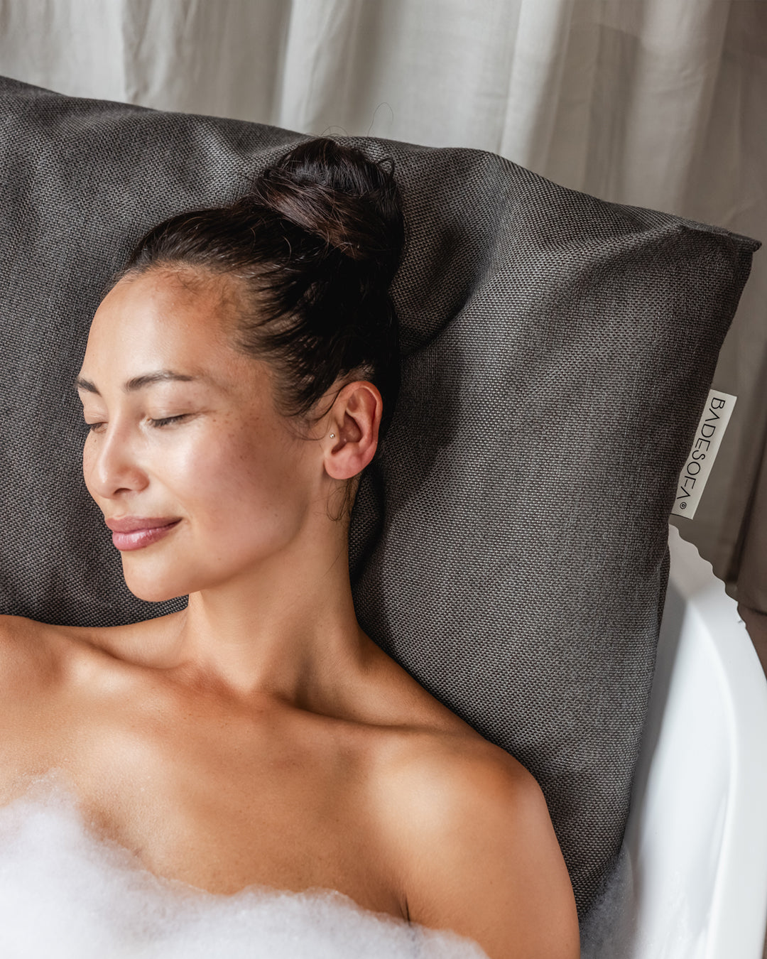 Mocha Badesofa Rückenkissen (Size Large) in einer freistehenden Badewanne, mit lächelnder Person, die sich entspannt anlehnt.