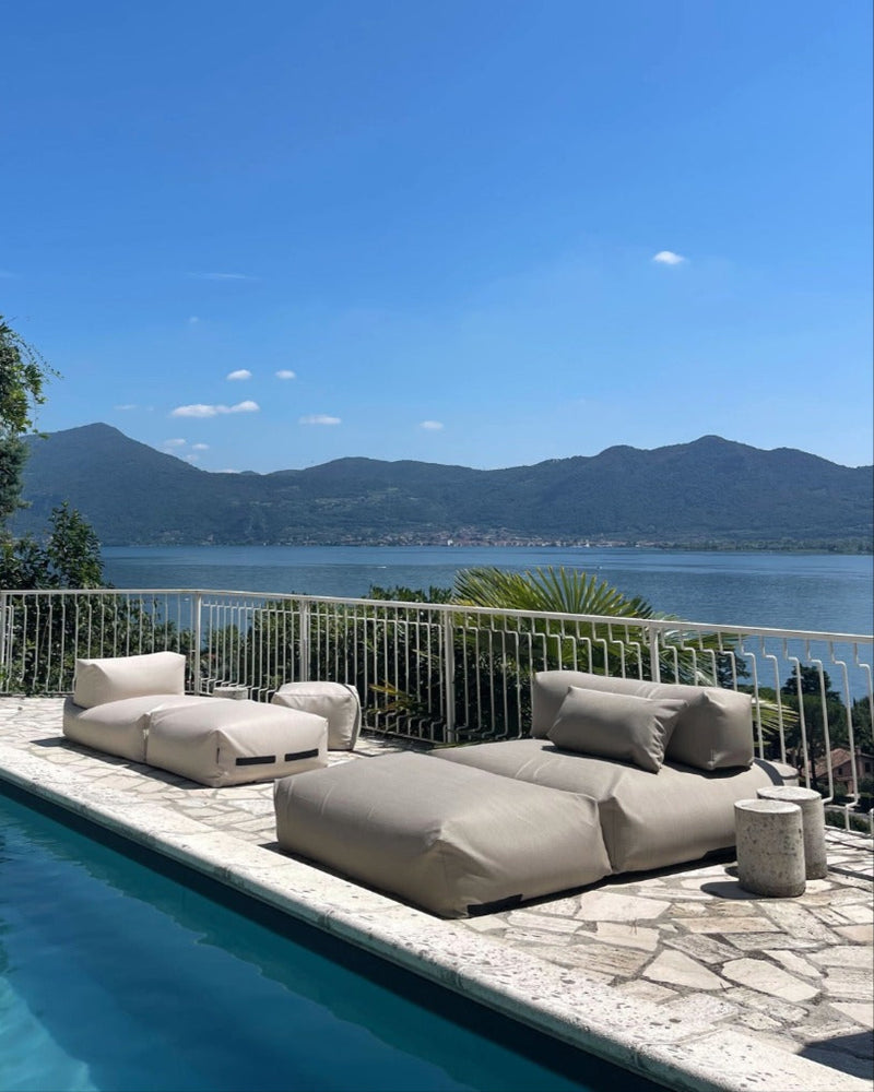 An einem Pool stehen zwei Poolsofas (ein Double in Beige, ein Single in Perlmutt) zusammen und ein Pouf in Small ist als Tisch dazugestellt. 